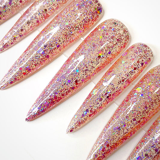 XXL stiletto press-on nails fully coated in pink-silver iridescent glitter and glossy topcoat pointed down towards the lower left of the frame